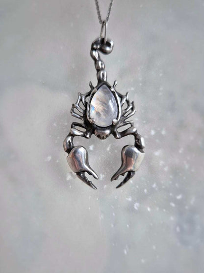 Front-facing image of handcrafted Scorpion necklace, rainbow moonstone center glowing, artisan silver jewelry display.