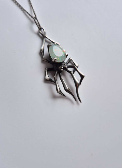 Artisan silver spider necklace with opal, tilted sideways on gradient background