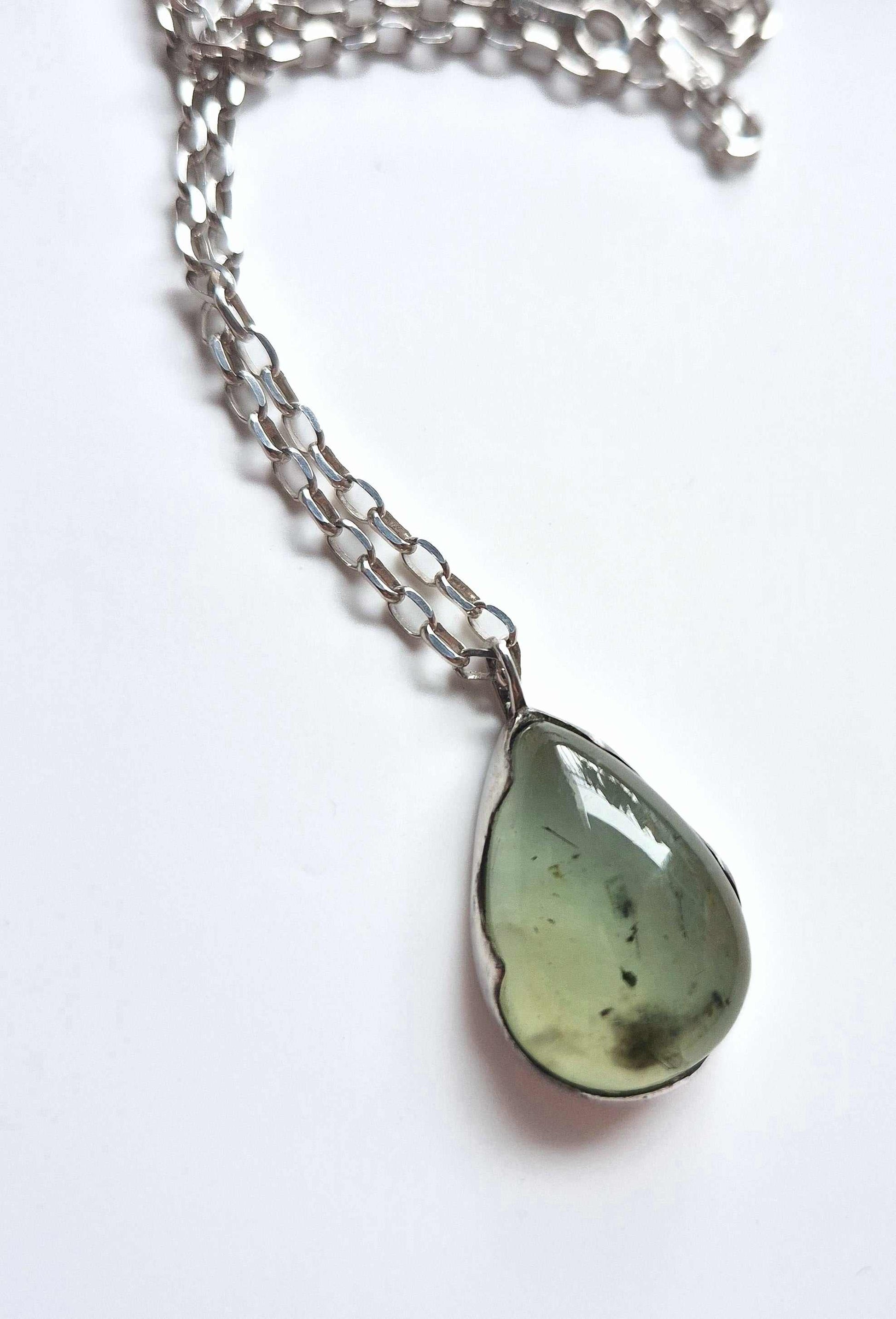 Close-up of prehnite pendant with silver chain loosely coiled