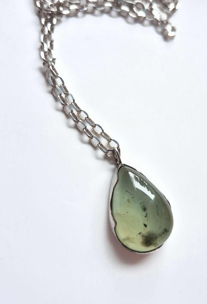 Close-up of prehnite pendant with silver chain loosely coiled