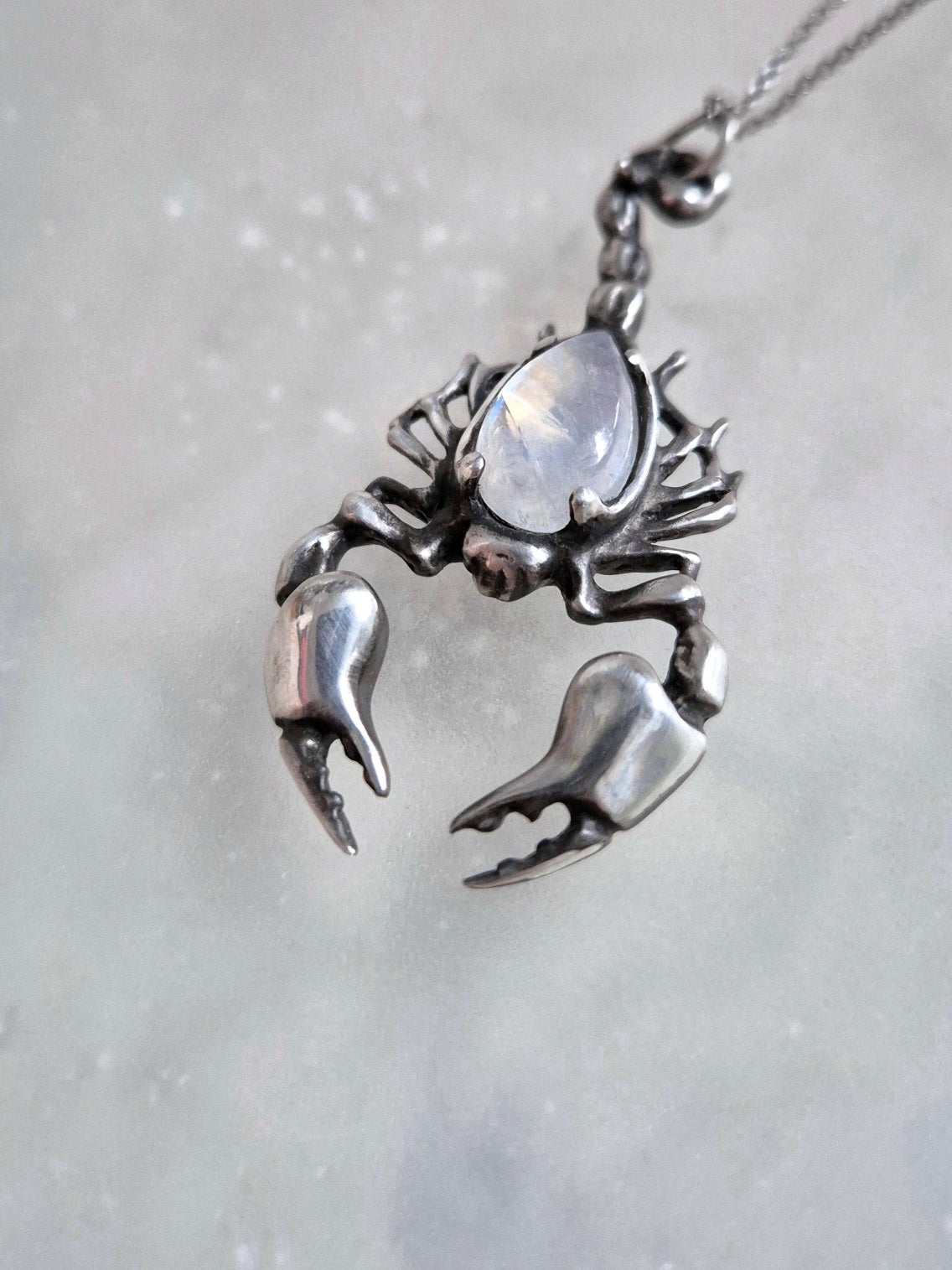 Angled shot of oxidized silver Scorpion pendant with shimmering rainbow moonstone, chain draped downward.