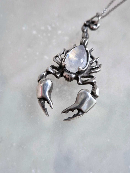 Angled shot of oxidized silver Scorpion pendant with shimmering rainbow moonstone, chain draped downward.