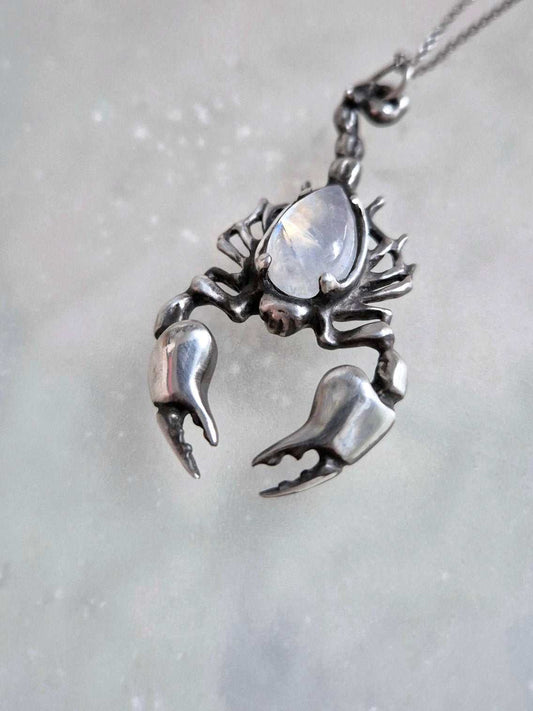 Angled shot of oxidized silver Scorpion pendant with  rainbow moonstone, chain draped downward.