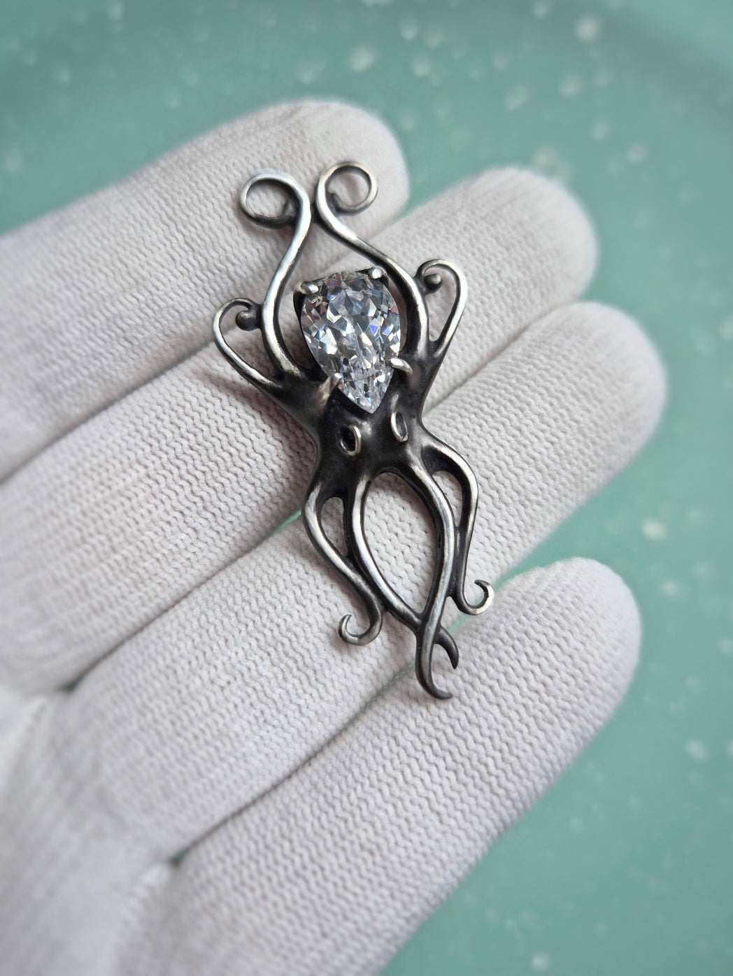 Silver octopus necklace with zircon gemstone displayed on in a gloved hand