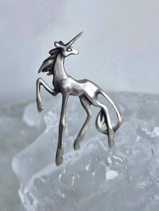Close-up of the sculpted sterling silver unicorn pendant standing on translucent glass