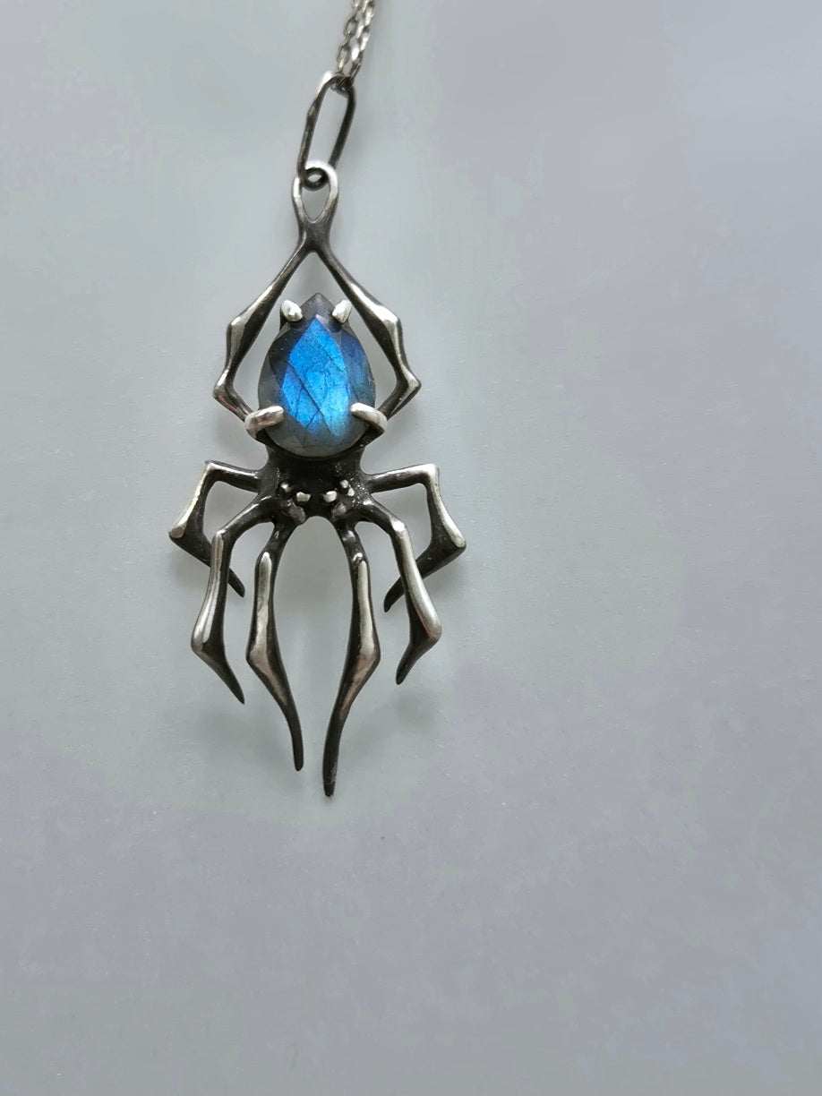 Silver spider necklace with vibrant blue labradorite gemstone on plain backdrop