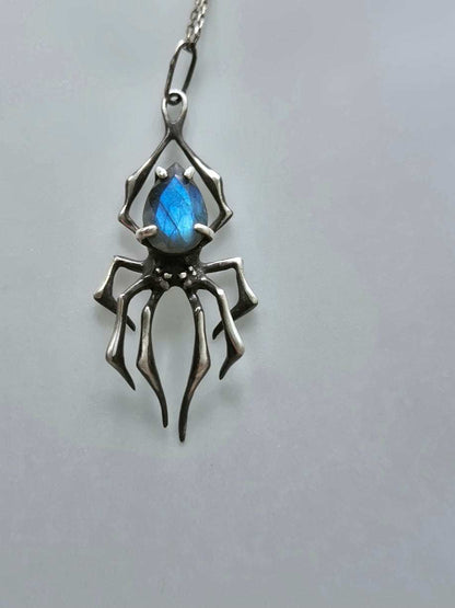 Silver spider necklace with vibrant blue labradorite gemstone on plain backdrop