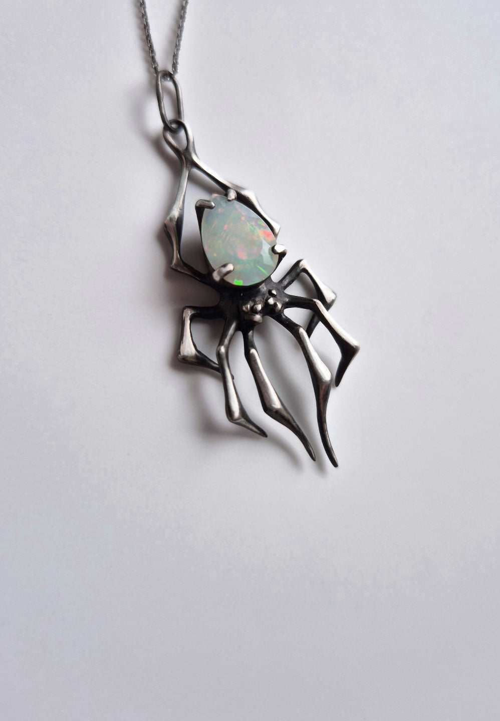 Close-up of silver spider talisman with opal, suspended on chain, minimalist backdrop