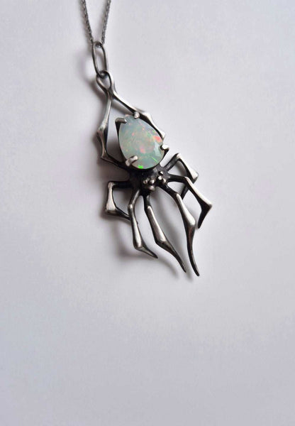 Close-up of silver spider talisman with opal, suspended on chain, minimalist backdrop