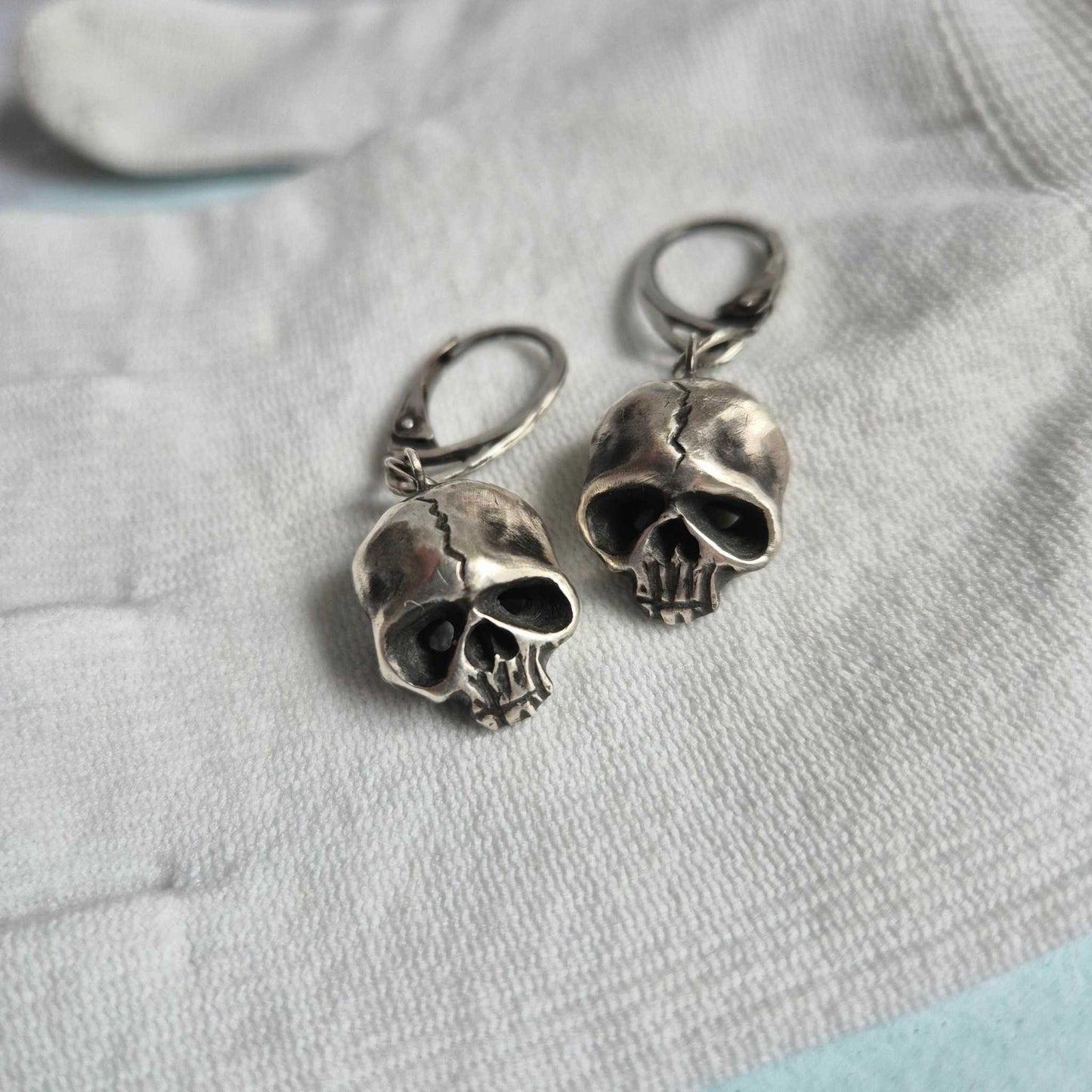 Skull earrings laying flat on textured surface