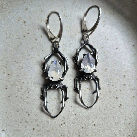 Pair of oxidized silver Spider earrings with moonstones, flat lay on light surface