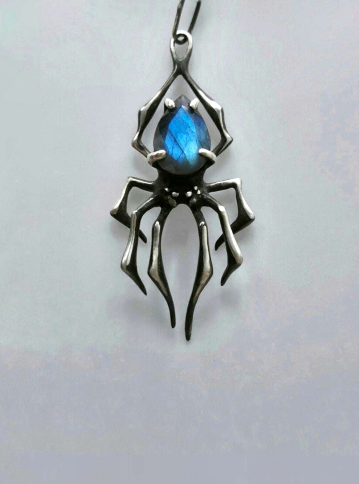 Front view of an oxidized sterling silver spider pendant with vivid blue labradorite on a pale gray background