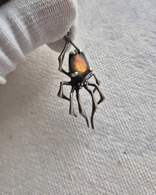 Silver spider necklace with a golden-flash labradorite, held delicately in a gloved hand