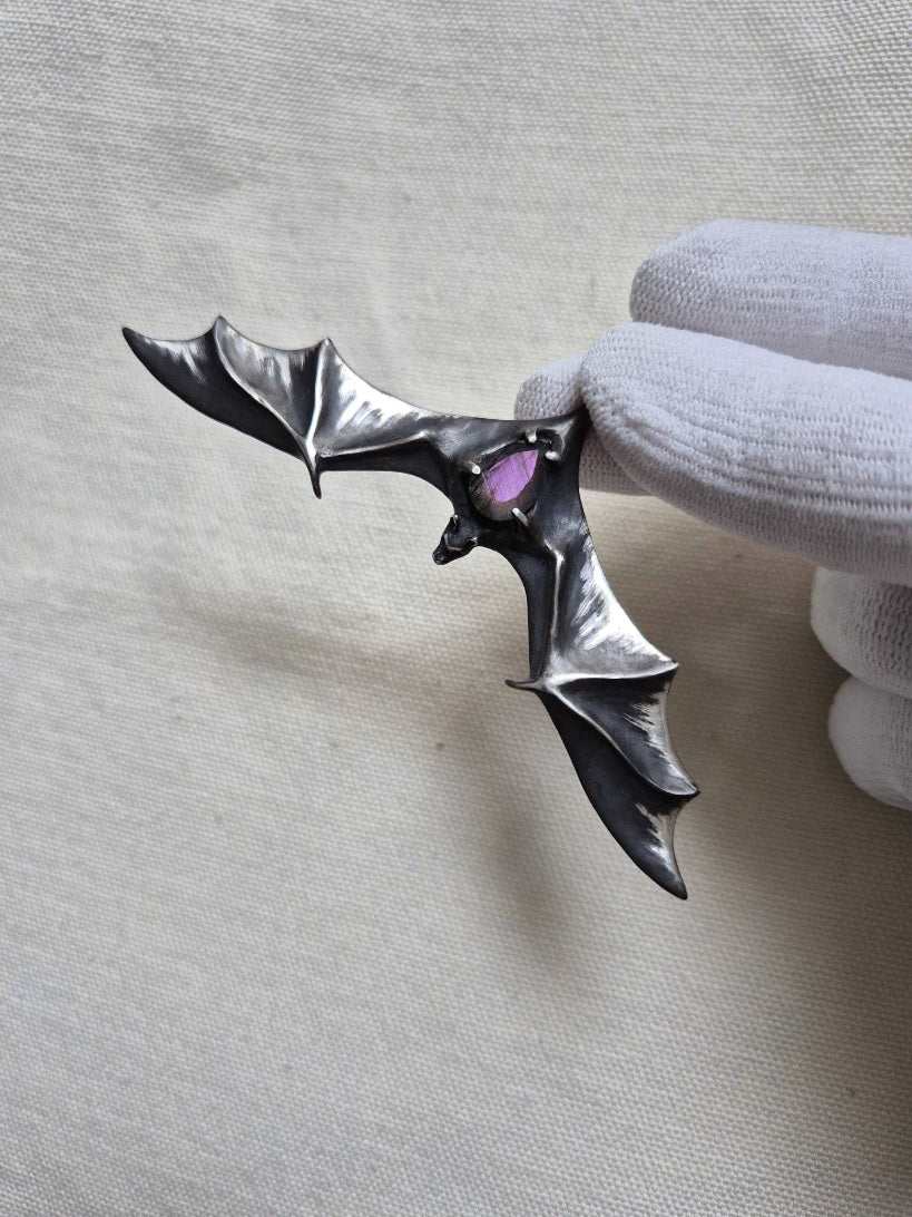 Silver Bat necklace with faceted labradorite gemstone, held in a gloved hand.
