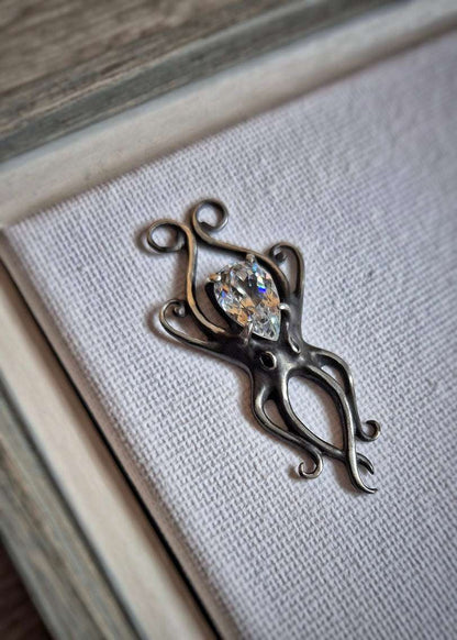 Silver octopus pendant resting on a textured surface, emphasizing detail and gemstone placement.