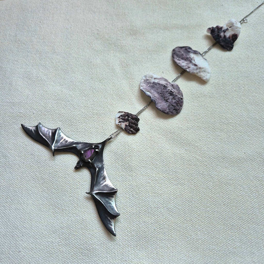 Sculptural silver Bat pendant with labradorite gem, laid out in full view on light fabric, and a chain decorated with seashells