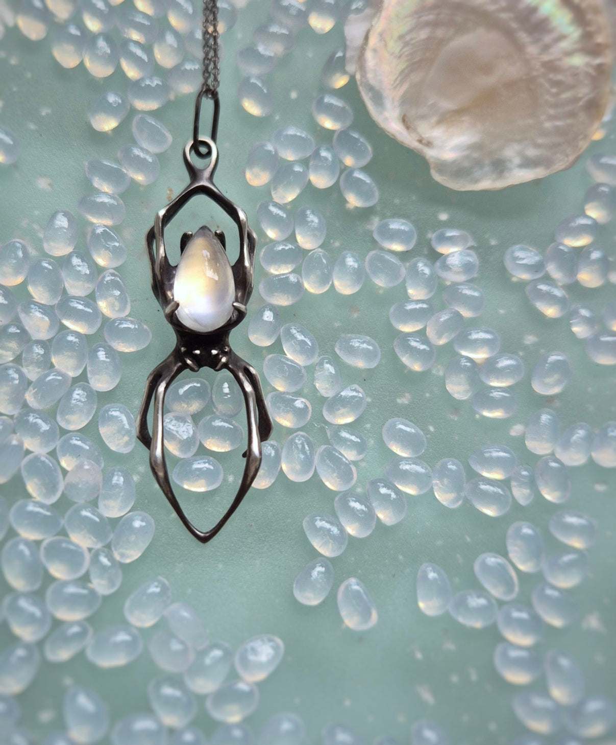Handmade silver spider necklace with moonstone, positioned on shimmering surface
