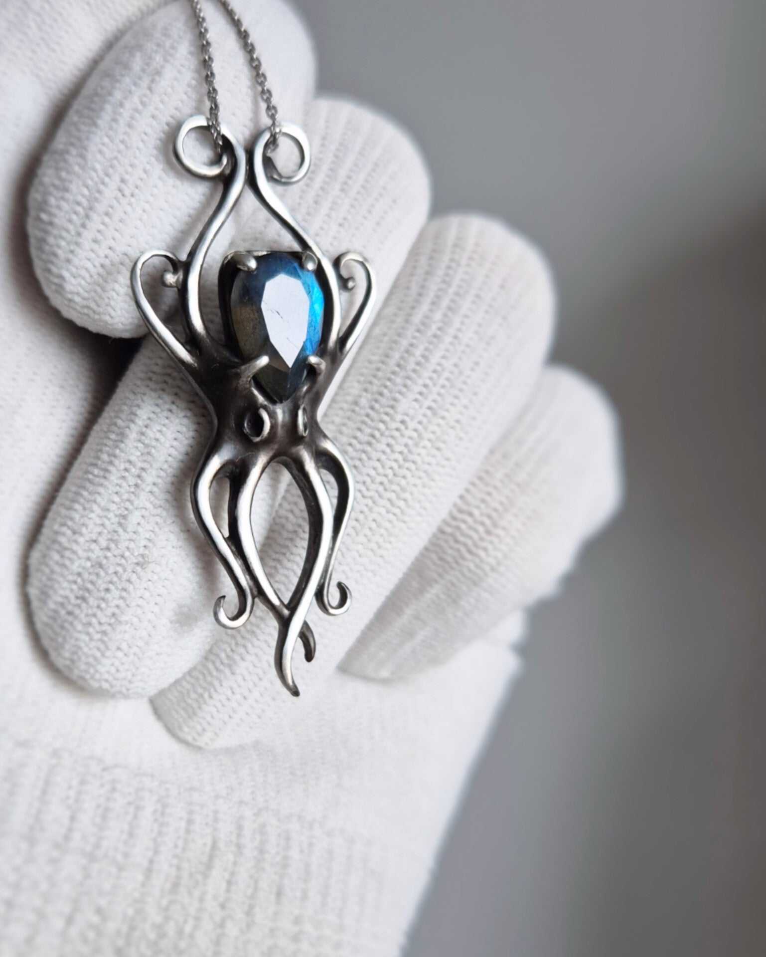Silver octopus necklace featuring bright blue stone, photographed in gloved hand against neutral background, artisan ocean talisman.