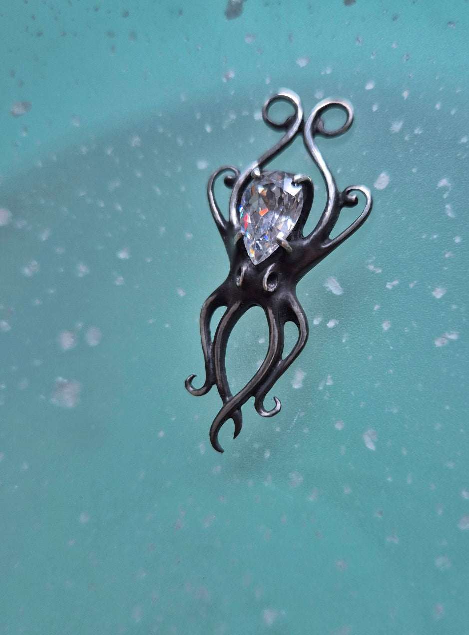 Handmade silver octopus necklace with zircon, positioned on blue background with glimmering water-like light.