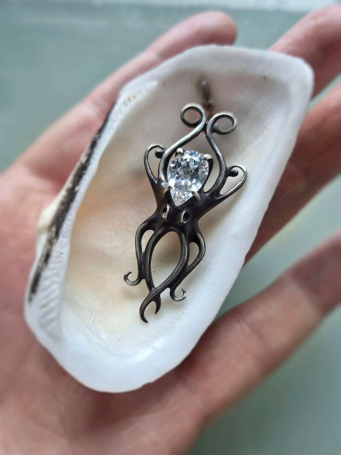 Octopus necklace in oxidized silver held in a white shell, showing sculptural tentacles and sparkling zircon.