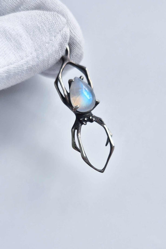 Close-up of an oxidized silver spider pendant with blue-flash rainbow moonstone held in a white-gloved hand