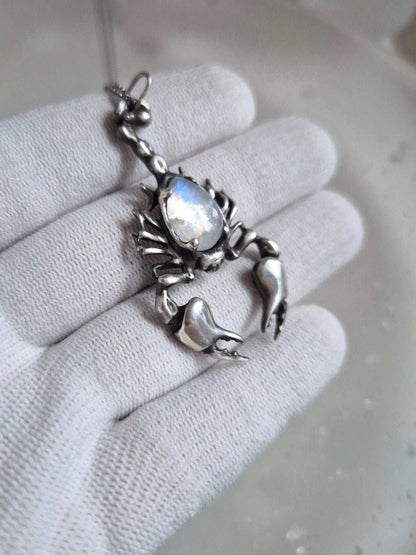 Close view of sterling-silver Scorpion pendant and iridescent rainbow moonstone cabochon resting on gloved palm.