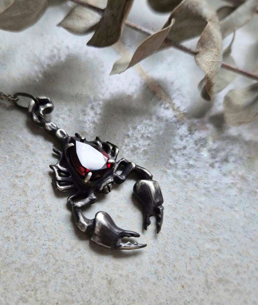 Scorpion necklace in Sterling Silver with Garnet gem, shot of neutral ceramic background
