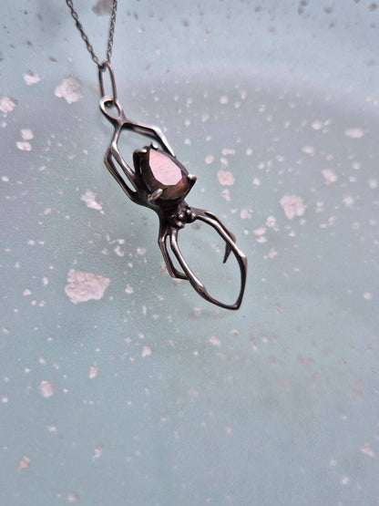 Handmade silver spider necklace with purple labradorite resting on a soft blue background with scattered highlights