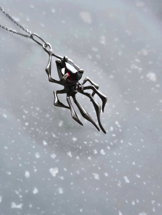 Angled view of artisan spider necklace in silver with glowing garnet gem