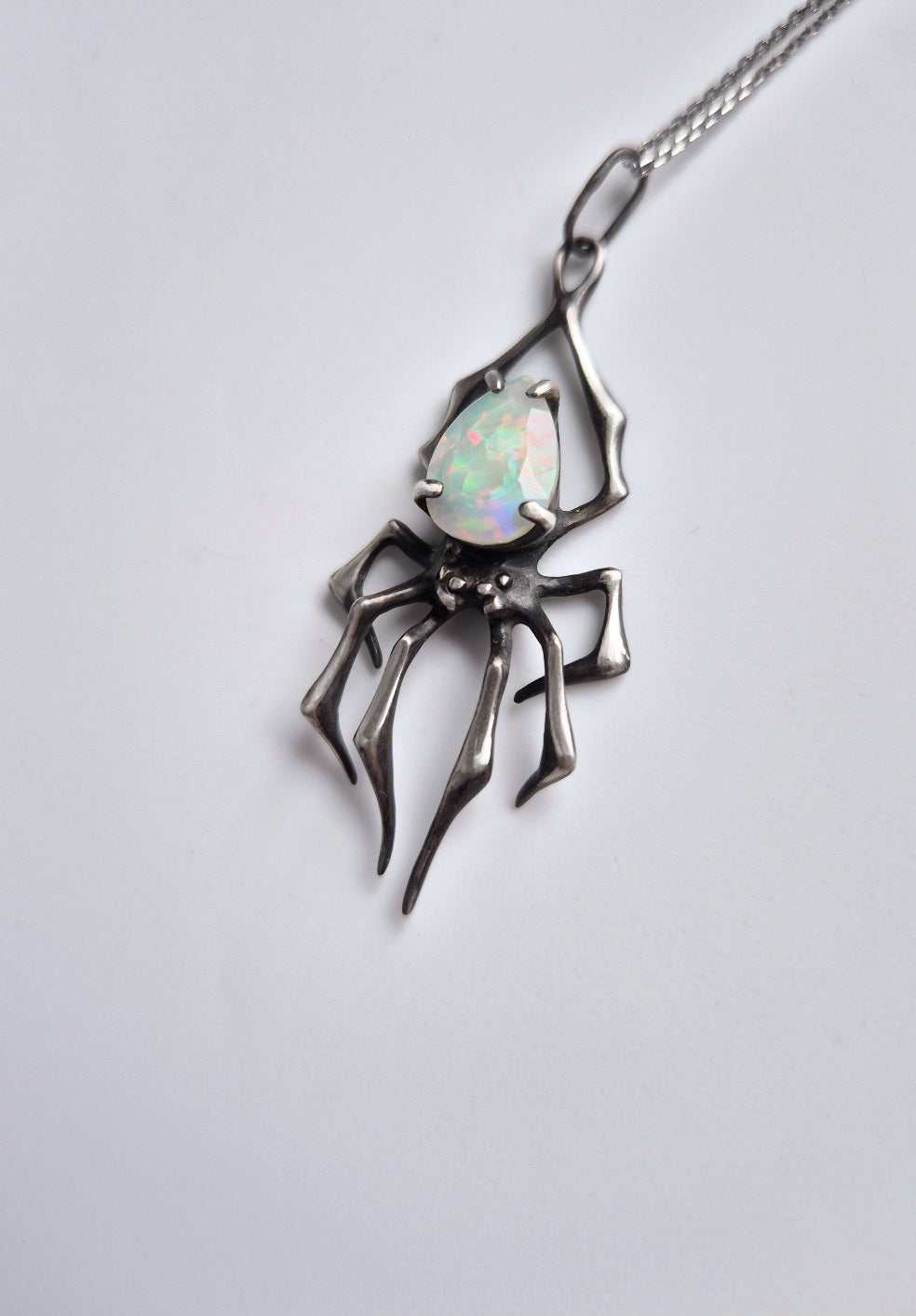 Silver spider-shaped pendant featuring opal gem, photographed from the left