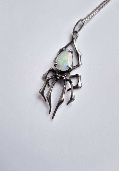 Silver spider-shaped pendant featuring opal gem, photographed from the left