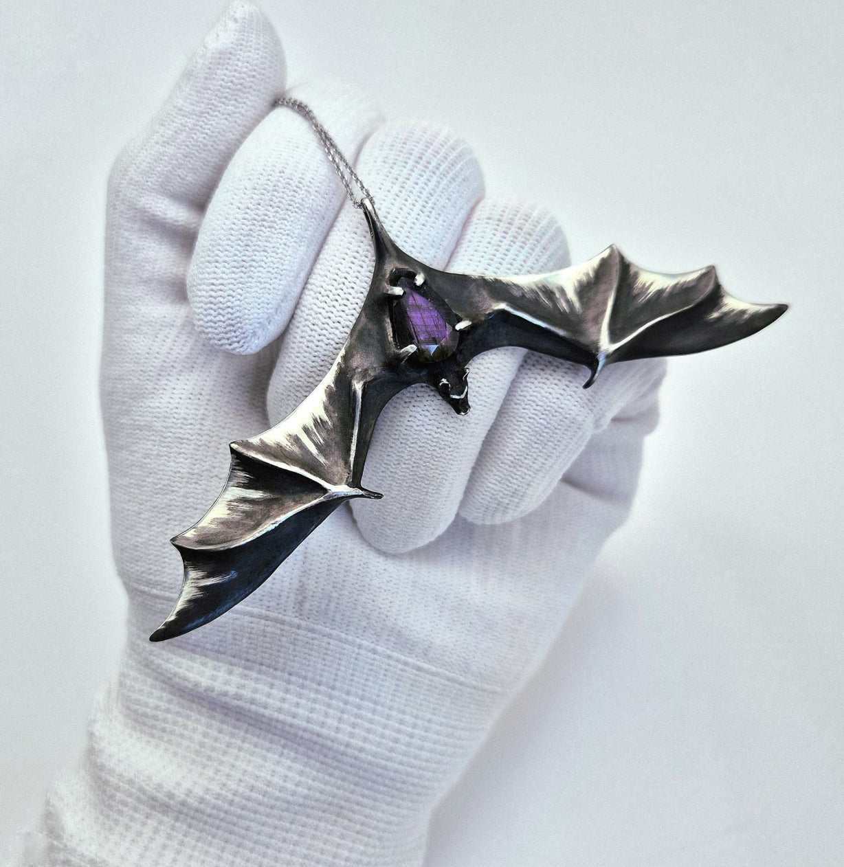 Silver Bat necklace with faceted labradorite gemstone, held in a gloved hand.