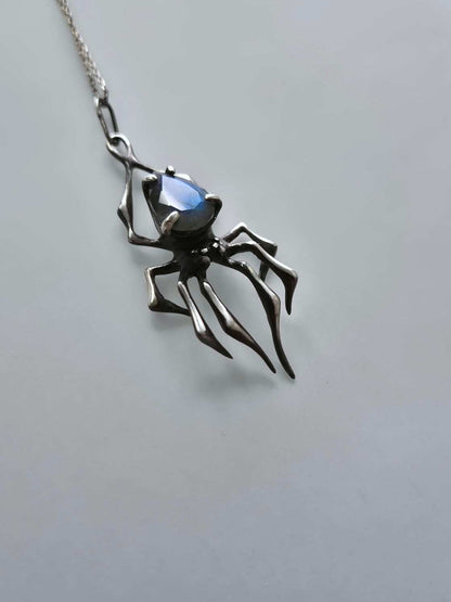 Angled view of silver spider necklace with glowing blue labradorite gem