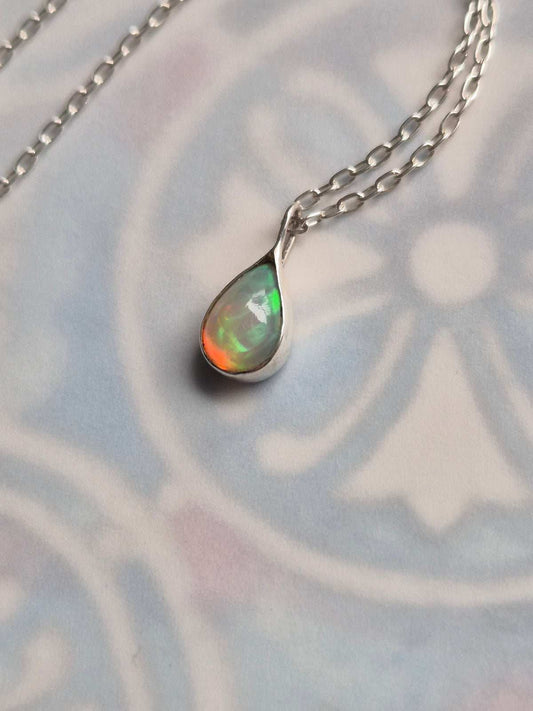 Close-up of Ethiopian opal pendant on silver chain, styled atop soft patterned paper with delicate light