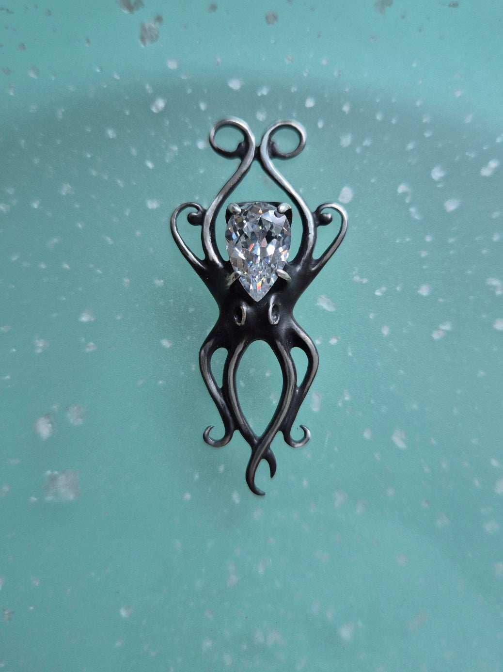 Silver octopus necklace with zircon gemstone displayed on a soft teal background