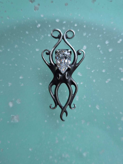 Silver octopus necklace with zircon gemstone displayed on a soft teal background
