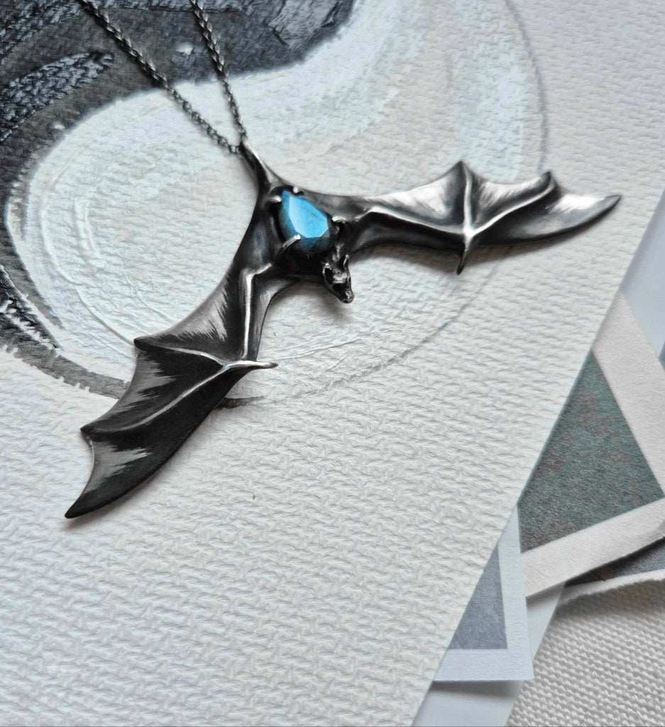 Handcrfted bat sterling silver necklace with vibrant blue stone, styled on angled display card