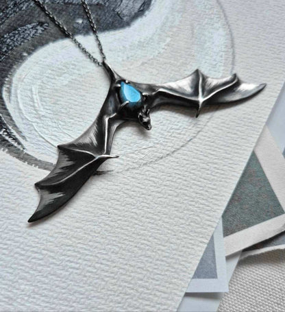 Handcrfted bat sterling silver necklace with vibrant blue stone, styled on angled display card