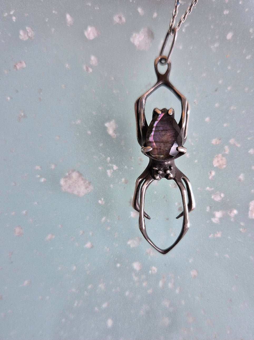 Close-up of the spider necklace featuring a purple labradorite, suspended from a silver chain.