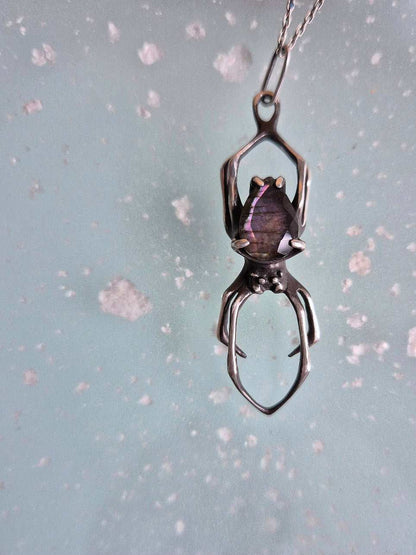 Close-up of the spider necklace featuring a purple labradorite, suspended from a silver chain.
