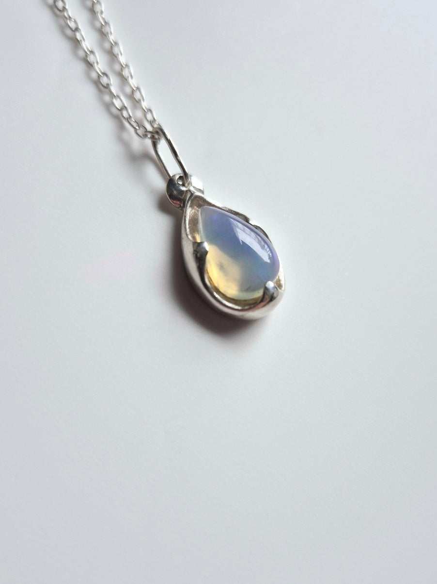 Teardrop-shaped opal pendant in sterling silver setting, shimmering blue tones, shown on a simple chain