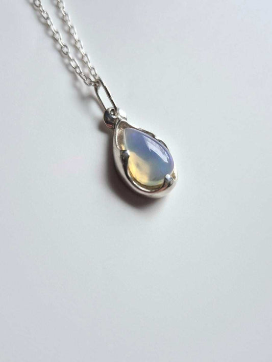 Teardrop-shaped opal pendant in sterling silver setting, shimmering blue tones, shown on a simple chain
