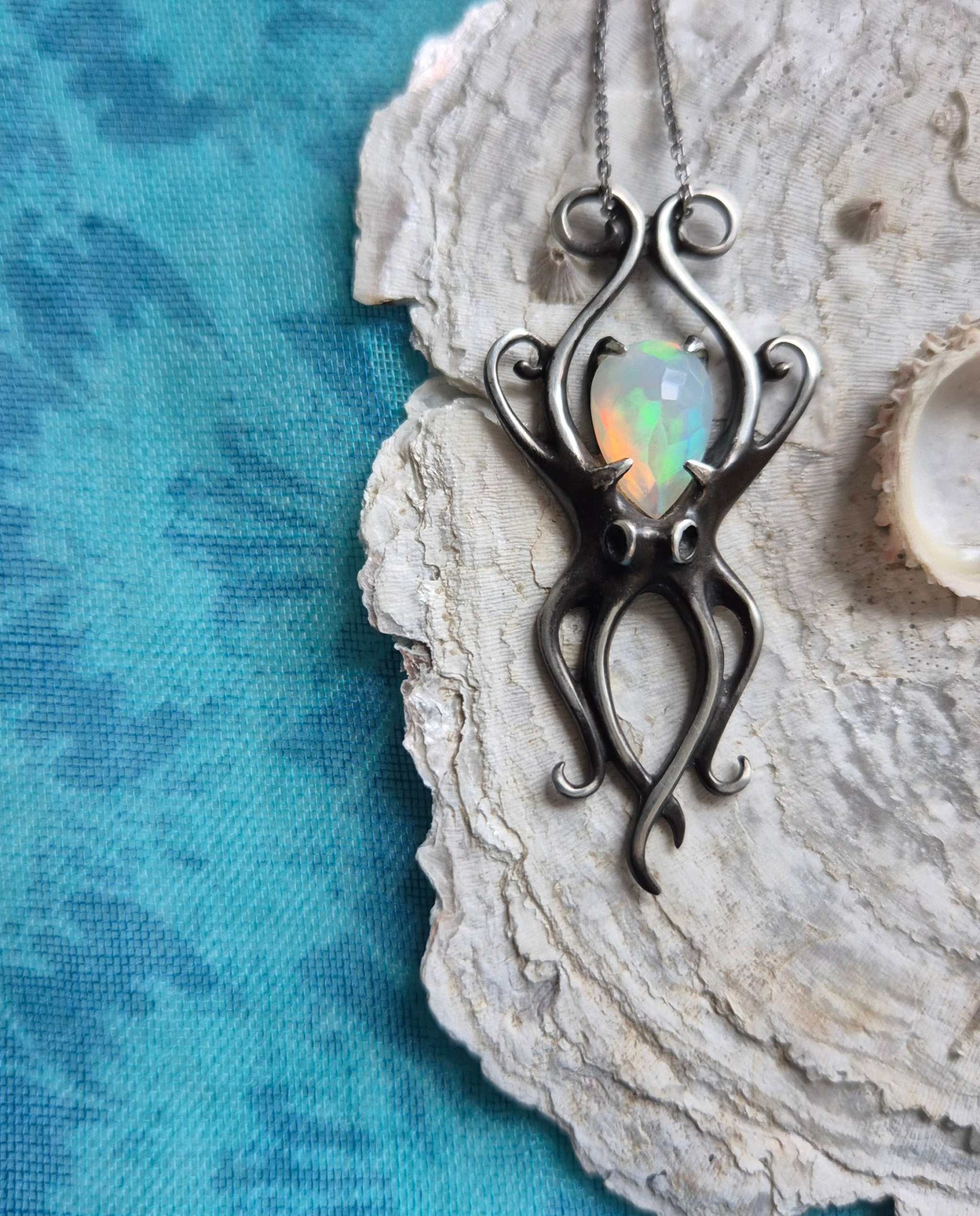 Silver octopus necklace with natural opal displayed on textured seashell, set against a vivid blue background