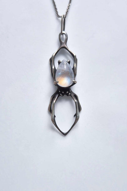 Front view of an oxidized sterling silver spider necklace with rainbow moonstone and chain on white