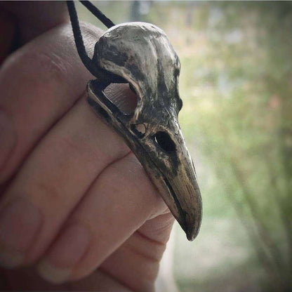 Artisan raven skull necklace held in hand outdoors.